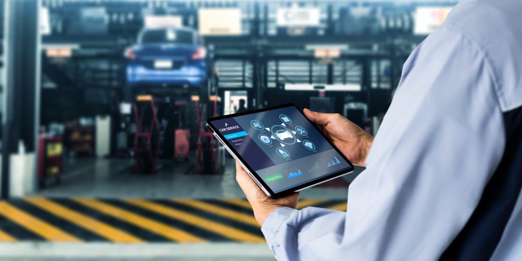 A technician using a tablet to access car service diagnostics in a garage.